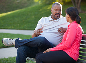 Man and woman sitting on park bench, talking.