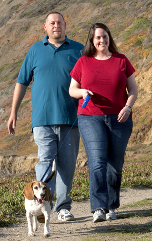 Man and woman outdoors walking a dog.