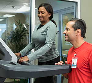Woman on treadmill being coached by physical therapist.